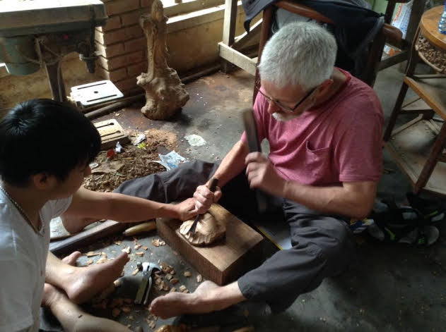 Một vị khách du lịch nước ngoài đang được hướng dẫn đẽo khắc gỗ tại làng mộc Kim Bồng. 